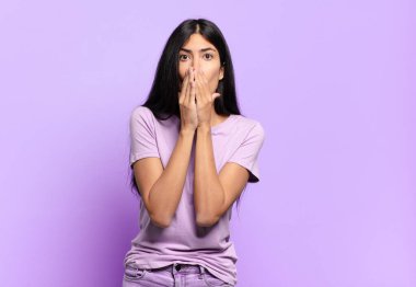 Genç, güzel, İspanyol bir kadın endişeli, üzgün ve korkmuş hissediyor. Ağzını ellerle kapatıyor. Endişeli ve berbat görünüyor.