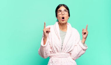 Şok olmuş, şaşırmış ve ağzı açık genç bir kadın. İki elini de havaya kaldırıp boşluğu dolduruyor. pijama konsepti
