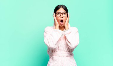 Genç ve güzel bir kadın hoş olmayan bir şekilde şok olmuş, korkmuş ya da endişeli görünüyor ağzı sonuna kadar açık ve iki kulağını da elleriyle kapatıyor. pijama konsepti