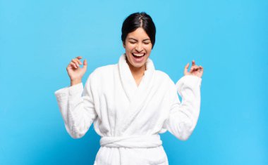 Genç İspanyol kadın son derece mutlu ve şaşırmış görünüyor, başarıyı kutluyor, bağırıyor ve zıplıyor. Bornoz konsepti