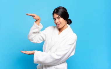 Bir objeyi gösteren, sunan ya da reklamını yapan, iki eli yanda olan genç bir İspanyol kadın. Bornoz konsepti