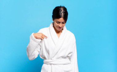 Genç İspanyol kadın neşeli ve sıradan bir şekilde gülümsüyor, aşağıya bakıyor ve göğsünü işaret ediyor. Bornoz konsepti