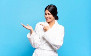 Genç İspanyol kadın neşeyle gülümsüyor ve bir objeyi gösteren ya da reklamını yapan avucundaki fotokopi alanını işaret ediyor. Bornoz konsepti