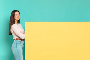 Genç ve güzel bir kadın kameraya çapraz kollarıyla gülümsüyor ve mutlu, kendinden emin, tatmin olmuş bir ifade, yan görüş. Konseptinizi yerleştirmek için boşluk kopyalayın