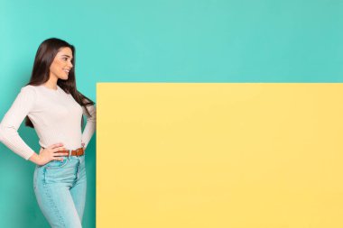 Genç, güzel bir kadın mutlu, neşeli ve kendinden emin görünüyor. Gururla gülümsüyor ve iki elini de kalçasında görmek istiyor. Konseptinizi yerleştirmek için boşluk kopyalayın