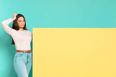 Genç, güzel bir kadın şaşkın ve kafası karışmış hissediyor. Kafasını kaşıyor ve yan tarafa bakıyor. Konseptinizi yerleştirmek için boşluk kopyalayın