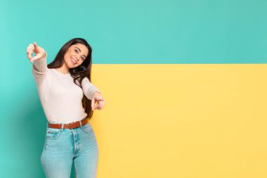 Genç ve güzel bir kadın mutlu ve kendinden emin, kamerayı iki eliyle gösteriyor ve gülüyor, seni seçiyor. Konseptinizi yerleştirmek için boşluk kopyalayın