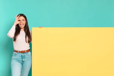 Genç ve güzel bir kadın mutlu bir şekilde gülümsüyor, şaka yapıyor ve gözetleme deliğinden bakıyor, sırları gözetliyor. Konseptinizi yerleştirmek için boşluk kopyalayın