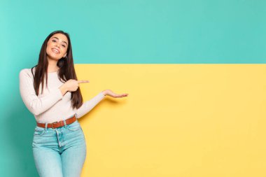 Genç, güzel bir kadın gülümsüyor, mutlu, kaygısız ve tatmin olmuş hissediyor, fotokopi alanındaki konsepte ya da fikre işaret ediyor. Konseptinizi yerleştirmek için boşluk kopyalayın