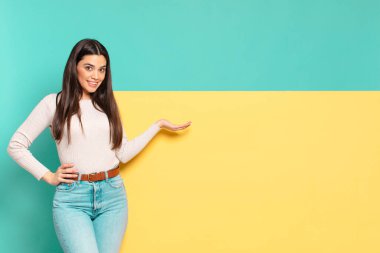 Genç, güzel bir kadın gülümsüyor, kendinden emin, başarılı ve mutlu hissediyor, fotokopi alanında fikir veya konsept gösteriyor. Konseptinizi yerleştirmek için boşluk kopyalayın