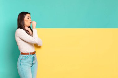 Gırtlağı ağrıyan ve grip belirtileri gösteren, ağzı kapalı öksüren genç ve güzel bir kadın. Konseptinizi yerleştirmek için boşluk kopyalayın