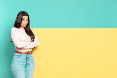 young pretty woman shrugging, feeling confused and uncertain, doubting with arms crossed and puzzled look. copy space to place your concept