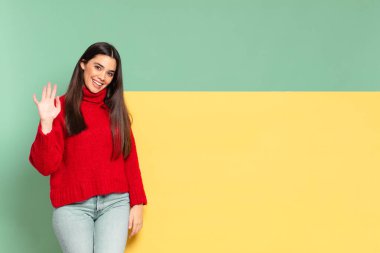young pretty woman smiling happily and cheerfully, waving hand, welcoming and greeting you, or saying goodbye. copy space to place your concept