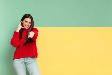 young pretty woman smiling cheerfully and pointing to camera while making a call you later gesture, talking on phone. copy space to place your concept