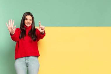 young pretty woman smiling and looking friendly, showing number seven or seventh with hand forward, counting down. copy space to place your concept