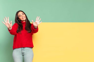 young pretty woman smiling and looking friendly, showing number ten or tenth with hand forward, counting down. copy space to place your concept