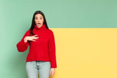 young pretty woman feeling shocked, astonished and surprised, with hand on chest and open mouth, saying who, me?. copy space to place your concept