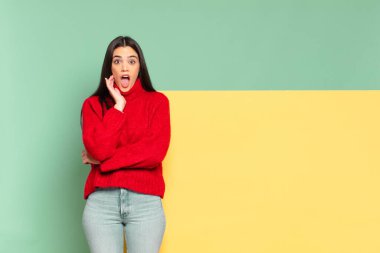 young pretty woman open-mouthed in shock and disbelief, with hand on cheek and arm crossed, feeling stupefied and amazed. copy space to place your concept