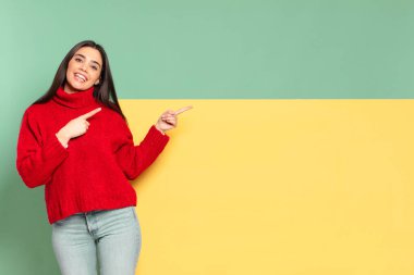young pretty woman smiling happily and pointing to side and upwards with both hands showing object in copy space. copy space to place your concept