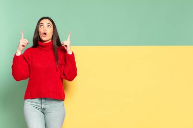 young pretty woman looking shocked, amazed and open mouthed, pointing upwards with both hands to copy space. copy space to place your concept