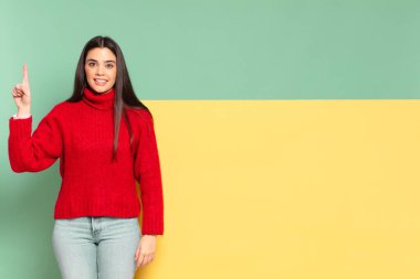 young pretty woman smiling cheerfully and happily, pointing upwards with one hand to copy space. copy space to place your concept