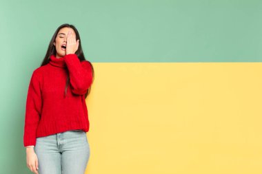 young pretty woman looking sleepy, bored and yawning, with a headache and one hand covering half the face. copy space to place your concept