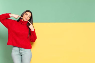 young pretty woman smiling confidently pointing to own broad smile, positive, relaxed, satisfied attitude. copy space to place your concept