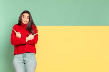 young pretty woman looking puzzled and confused, insecure and pointing in opposite directions with doubts. copy space to place your concept