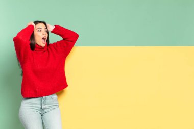 young pretty woman with open mouth, looking horrified and shocked because of a terrible mistake, raising hands to head. copy space to place your concept