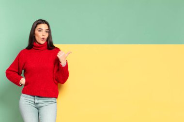 young pretty woman looking astonished in disbelief, pointing at object on the side and saying wow, unbelievable. copy space to place your concept