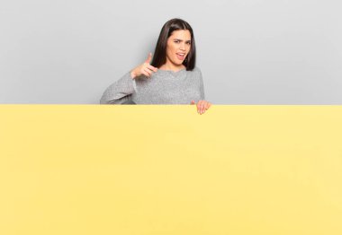 young pretty woman pointing at camera with an angry aggressive expression looking like a furious, crazy boss. copy space to place your concept