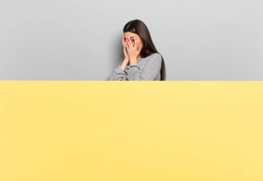 young pretty woman feeling scared or embarrassed, peeking or spying with eyes half-covered with hands. copy space to place your concept