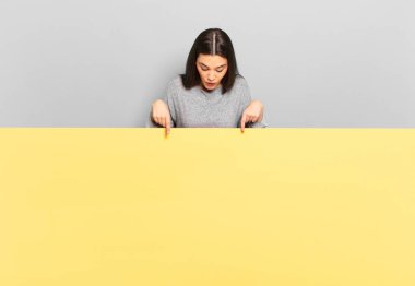 young pretty woman feeling awed and open mouthed pointing upwards with a shocked and surprised look. copy space to place your concept