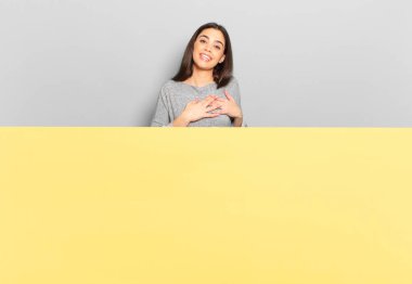 young pretty woman feeling romantic, happy and in love, smiling cheerfully and holding hands close to heart. copy space to place your concept