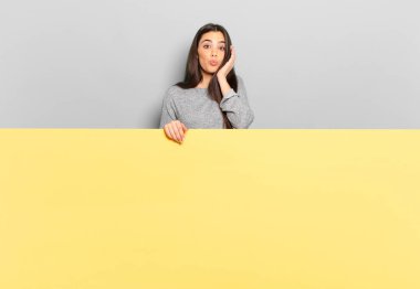 young pretty woman feeling shocked and astonished holding face to hand in disbelief with mouth wide open. copy space to place your concept