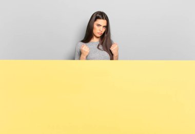 young pretty woman looking confident, angry, strong and aggressive, with fists ready to fight in boxing position. copy space to place your concept