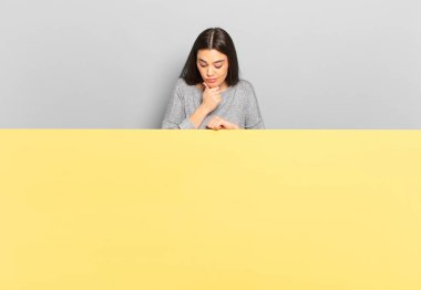 young pretty woman thinking, feeling doubtful and confused, with different options, wondering which decision to make. copy space to place your concept