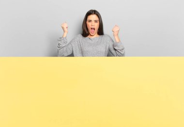 young pretty woman shouting aggressively with an angry expression or with fists clenched celebrating success. copy space to place your concept