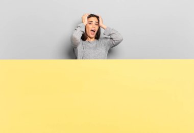 young pretty woman feeling horrified and shocked, raising hands to head and panicking at a mistake. copy space to place your concept