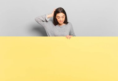 young pretty woman feeling clueless and confused, thinking a solution, with hand on hip and other on head, rear view. copy space to place your concept