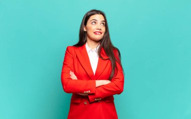 young pretty woman feeling happy, proud and hopeful, wondering or thinking, looking up to copy space with crossed arms. business concept