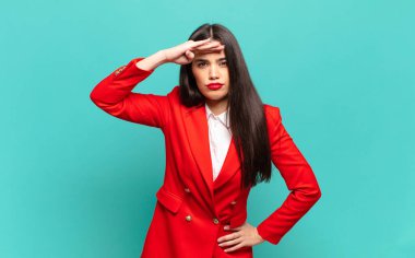 young pretty woman looking bewildered and astonished, with hand over forehead looking far away, watching or searching. business concept