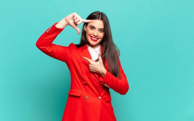 young pretty woman feeling happy, friendly and positive, smiling and making a portrait or photo frame with hands. business concept