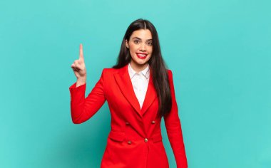 young pretty woman smiling cheerfully and happily, pointing upwards with one hand to copy space. business concept