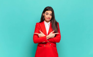 young pretty woman looking puzzled and confused, insecure and pointing in opposite directions with doubts. business concept
