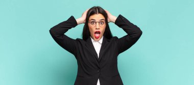 young pretty woman looking excited and surprised, open-mouthed with both hands on head, feeling like a lucky winner. business concept