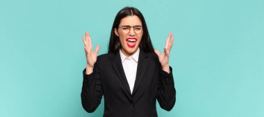 young pretty woman furiously screaming, feeling stressed and annoyed with hands up in the air saying why me. business concept