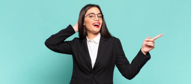 young pretty woman laughing, looking happy, positive and surprised, realizing a great idea pointing to lateral copy space. business concept