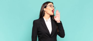 young pretty woman yelling loudly and angrily to copy space on the side, with hand next to mouth. business concept