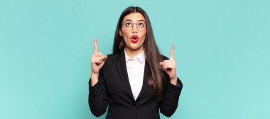 young pretty woman feeling awed and open mouthed pointing upwards with a shocked and surprised look. business concept